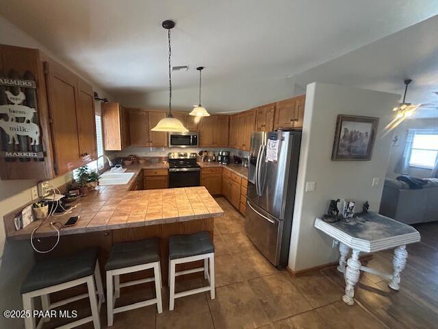 5575 N Debbie Ln, Rimrock, AZ 86335 - kitchen featuring stainless steel appliances, a sink, a peninsula, hanging light fixtures, and brown cabinetry
