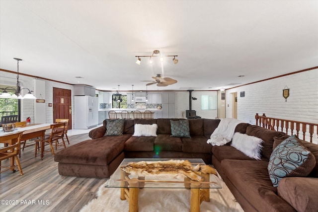 4937 S Deer Trl, Prescott, AZ 86303 - living area featuring a wood stove, brick wall, light wood-style flooring, ceiling fan, and ornamental molding
