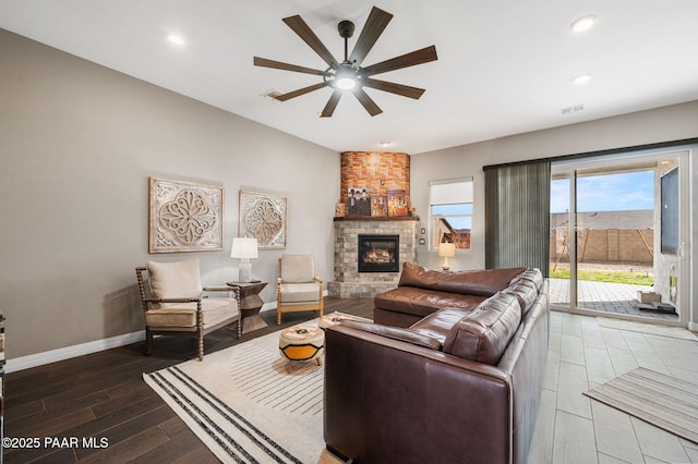 living room with wood-type flooring, a stone fireplace, and ceiling fan