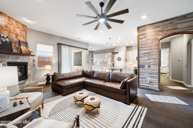 living room with dark hardwood / wood-style flooring, sink, a stone fireplace, and ceiling fan