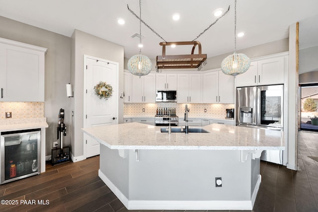 kitchen featuring light stone counters, hanging light fixtures, appliances with stainless steel finishes, beverage cooler, and white cabinets