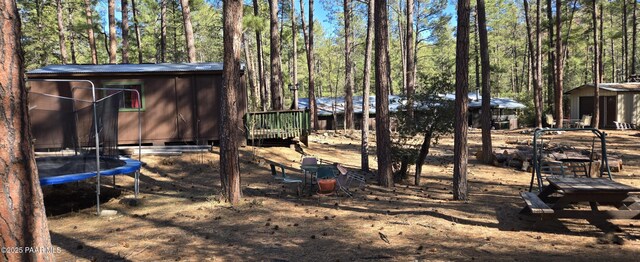view of yard featuring an outdoor structure, a wooded view, and a trampoline