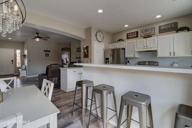 kitchen with ceiling fan with notable chandelier, a breakfast bar, white cabinets, and stainless steel refrigerator with ice dispenser