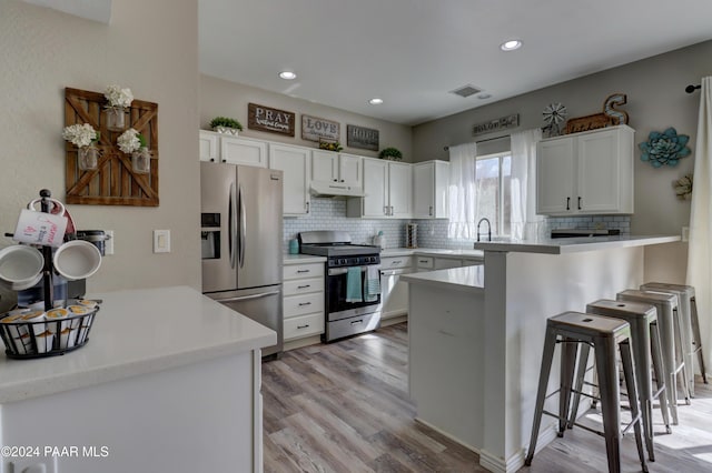 kitchen with a kitchen bar, kitchen peninsula, stainless steel appliances, light hardwood / wood-style floors, and white cabinetry