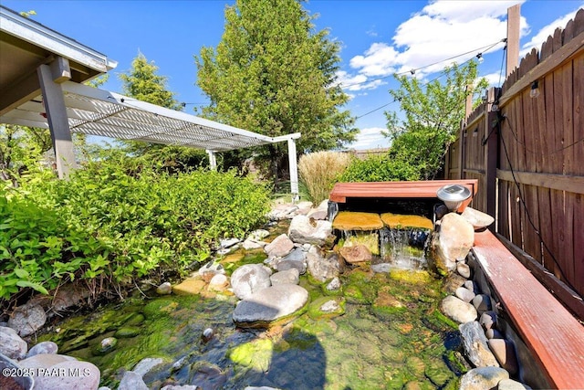 view of yard with a small pond, a pergola, and fence