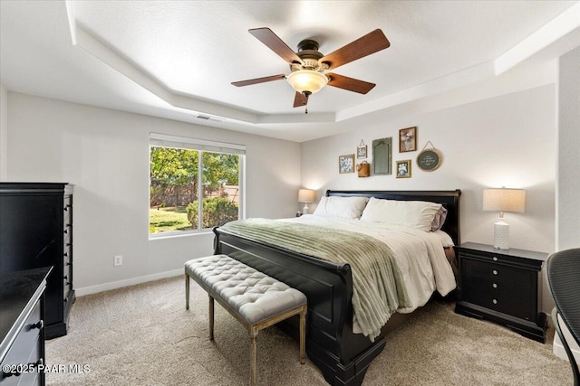 bedroom featuring a ceiling fan, visible vents, baseboards, light carpet, and a tray ceiling