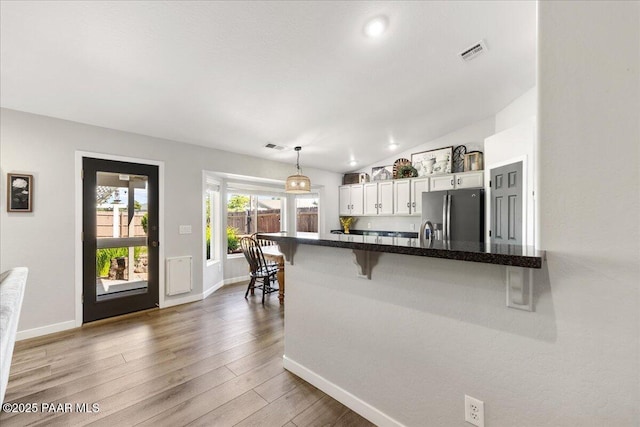 kitchen featuring white cabinets, stainless steel fridge with ice dispenser, a breakfast bar area, baseboards, and visible vents