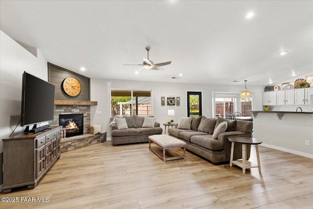 living room featuring ceiling fan, a fireplace, baseboards, light wood finished floors, and recessed lighting