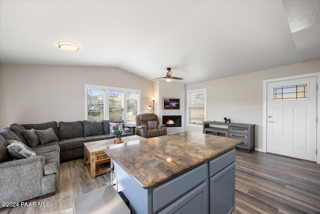 kitchen featuring a large fireplace, vaulted ceiling, ceiling fan, dark wood-type flooring, and a center island