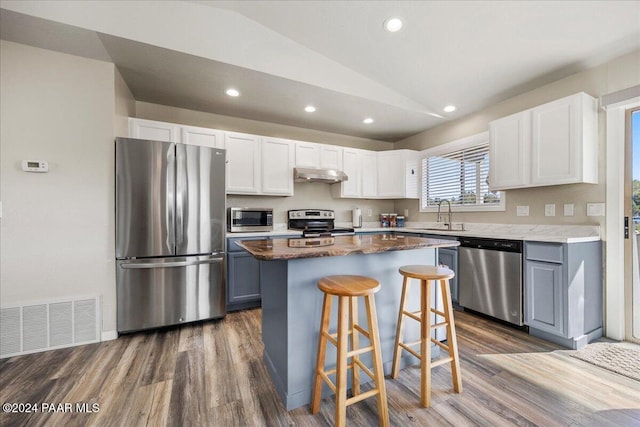 kitchen featuring a center island, lofted ceiling, a kitchen bar, white cabinets, and appliances with stainless steel finishes