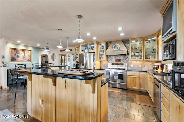 kitchen featuring appliances with stainless steel finishes, a kitchen breakfast bar, custom range hood, hanging light fixtures, and an island with sink