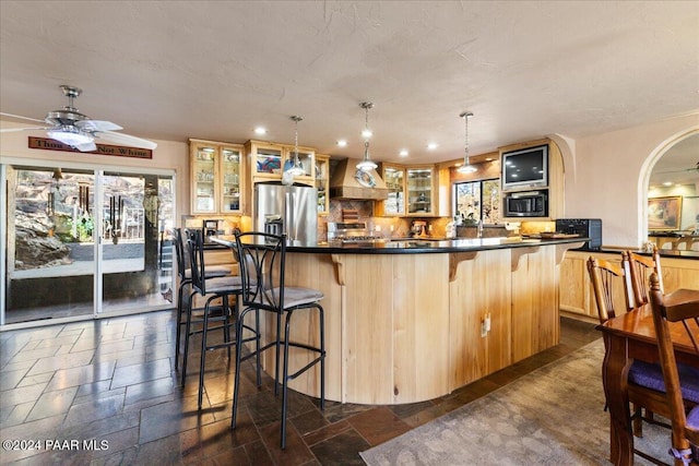 kitchen featuring ceiling fan, stainless steel appliances, decorative light fixtures, a breakfast bar area, and custom range hood