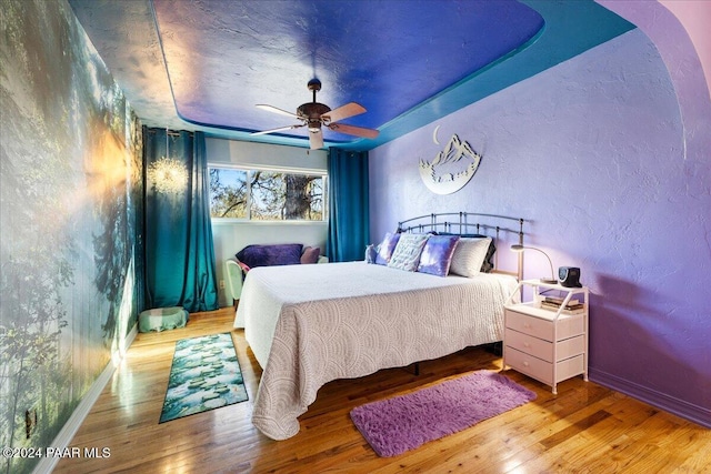 bedroom featuring hardwood / wood-style flooring, a raised ceiling, and ceiling fan