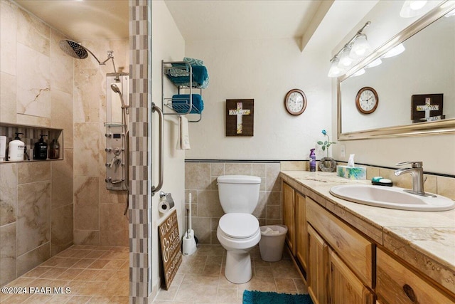 bathroom with a tile shower, vanity, toilet, and tile walls