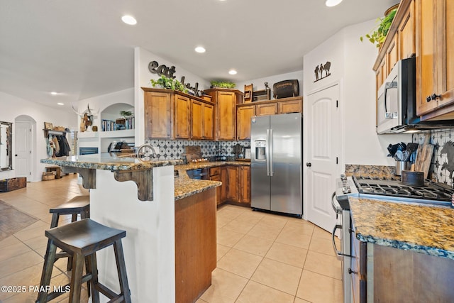 8950 N Calico Cat Trl, Prescott Valley, AZ 86315 - kitchen with stainless steel appliances, a peninsula, light tile patterned flooring, brown cabinetry, and recessed lighting
