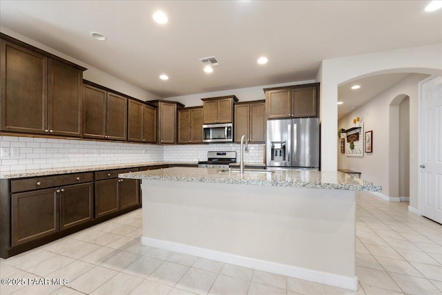 kitchen with light stone counters, appliances with stainless steel finishes, sink, and a center island with sink