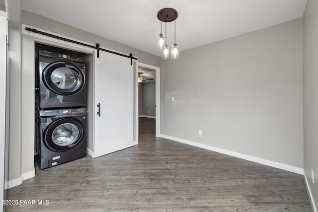 laundry room with stacked washer and dryer, ceiling fan, a barn door, and dark hardwood / wood-style flooring