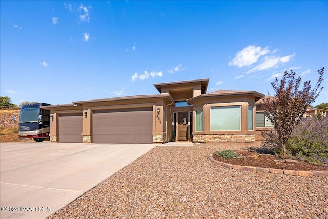 prairie-style house featuring stucco siding, stone siding, concrete driveway, and an attached garage