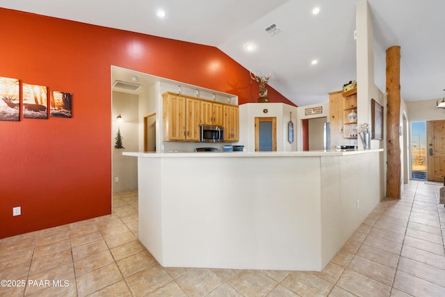 kitchen with light tile patterned flooring, light brown cabinets, kitchen peninsula, and lofted ceiling