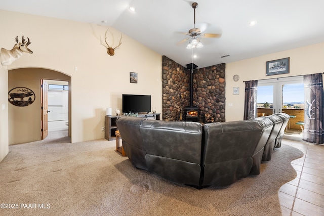 tiled living room with ceiling fan, a wood stove, and lofted ceiling