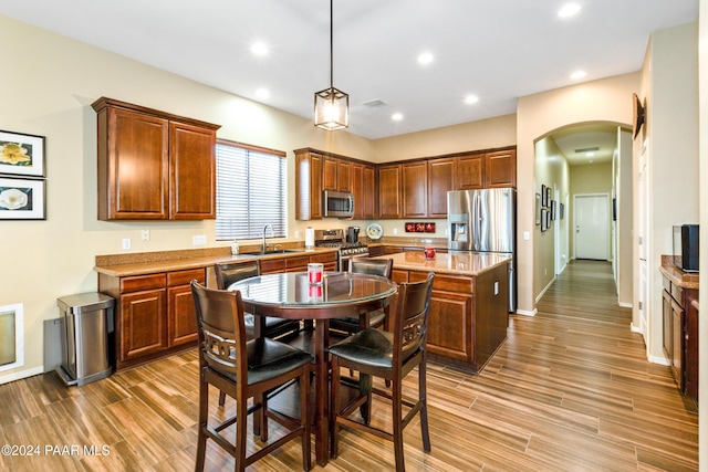 kitchen featuring sink, light stone counters, appliances with stainless steel finishes, a kitchen island, and pendant lighting