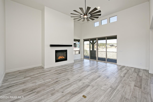 unfurnished living room with a high ceiling, ceiling fan, and light hardwood / wood-style floors