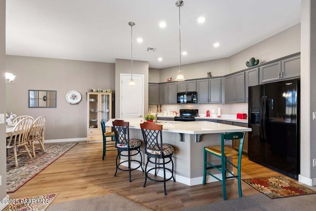 kitchen with gray cabinetry, decorative light fixtures, light hardwood / wood-style flooring, and black appliances