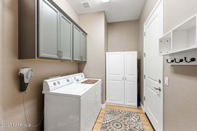 clothes washing area featuring cabinets, washing machine and clothes dryer, and light hardwood / wood-style floors