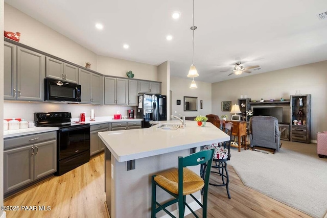 kitchen featuring gray cabinets, a breakfast bar, decorative light fixtures, a kitchen island with sink, and black appliances