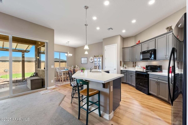 kitchen featuring gray cabinets, a breakfast bar area, hanging light fixtures, black appliances, and a center island with sink