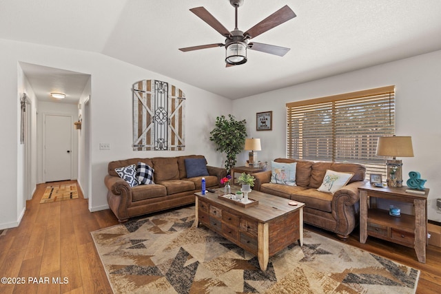 living area featuring baseboards, wood finished floors, ceiling fan, and vaulted ceiling