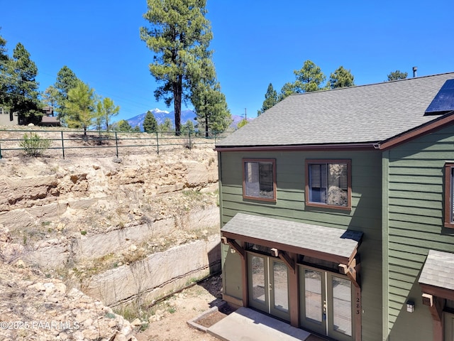 view of side of home with a mountain view, fence, and roof with shingles