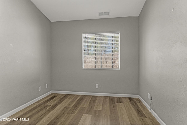 empty room with baseboards, visible vents, and wood finished floors