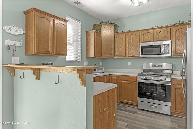 kitchen with light wood finished floors, stainless steel appliances, a breakfast bar, visible vents, and light countertops