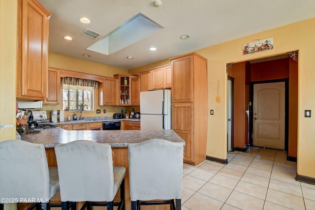 kitchen featuring a breakfast bar area, a peninsula, a skylight, freestanding refrigerator, and dishwasher