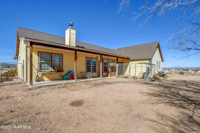 back of house with a gate, a chimney, and fence