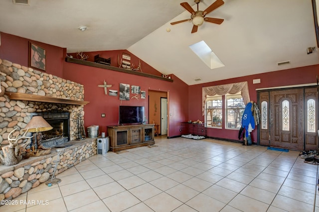 tiled living room featuring lofted ceiling with skylight, a fireplace, visible vents, and a ceiling fan