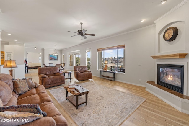 living room featuring light wood-type flooring, ceiling fan, crown molding, and a fireplace