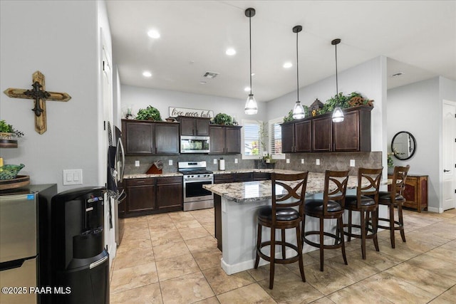 7123 E Roque Ln, Prescott Valley, AZ 86315 - kitchen with appliances with stainless steel finishes, decorative backsplash, dark brown cabinetry, a kitchen bar, and recessed lighting