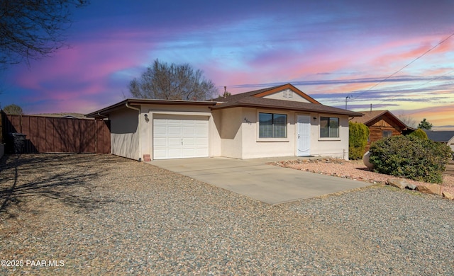 ranch-style house featuring driveway, a garage, fence, and stucco siding