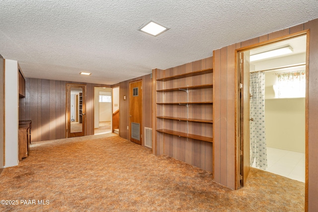 unfurnished living room with light colored carpet, a textured ceiling, and wood walls