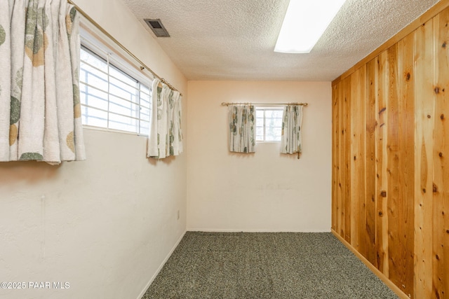 carpeted empty room with wooden walls and a textured ceiling