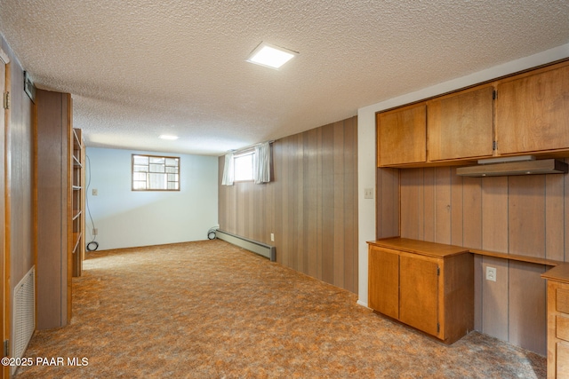 basement with built in desk, wood walls, light colored carpet, baseboard heating, and a textured ceiling