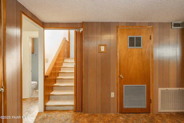 stairs featuring carpet flooring, a textured ceiling, and wood walls