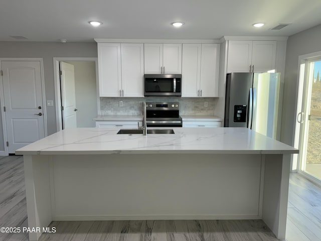 kitchen with tasteful backsplash, a center island with sink, visible vents, appliances with stainless steel finishes, and white cabinetry