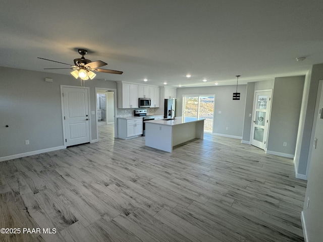 kitchen featuring a center island with sink, white cabinets, appliances with stainless steel finishes, open floor plan, and light countertops