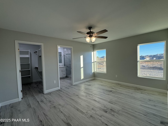 unfurnished bedroom with light wood-style flooring, a ceiling fan, baseboards, a spacious closet, and a closet