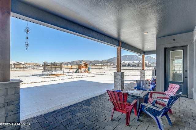 snow covered patio with a trampoline, a mountain view, and a playground