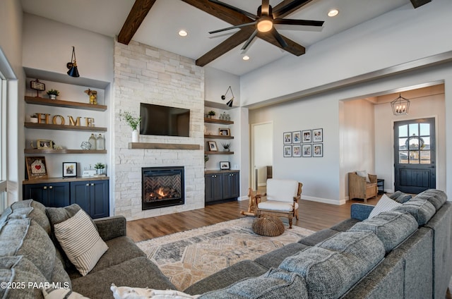 living room featuring a stone fireplace, built in shelves, dark hardwood / wood-style floors, and beamed ceiling