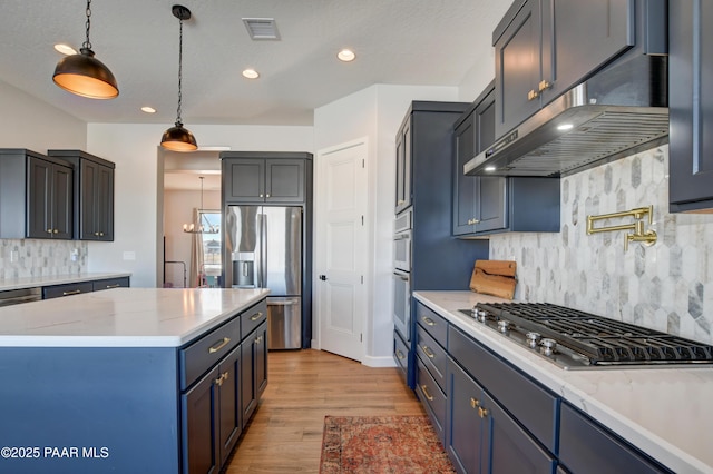 kitchen featuring stainless steel appliances, a kitchen island, decorative light fixtures, wall chimney exhaust hood, and light wood-type flooring